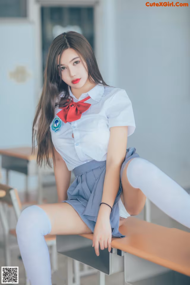 A woman in a school uniform sitting on a desk.