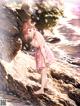 A woman in a pink dress standing on a rock by the water.