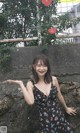 A woman in a black dress standing next to a stone wall.