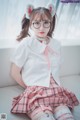 A woman in a white shirt and pink plaid skirt sitting on a white couch.