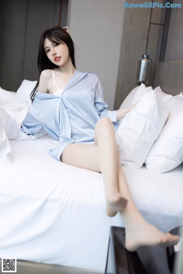 A woman sitting on top of a bed in a blue shirt.