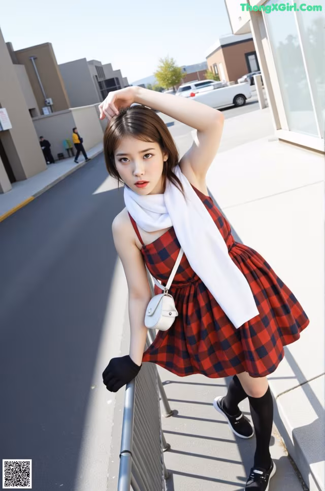 A woman in a red and black plaid dress leaning against a fence.