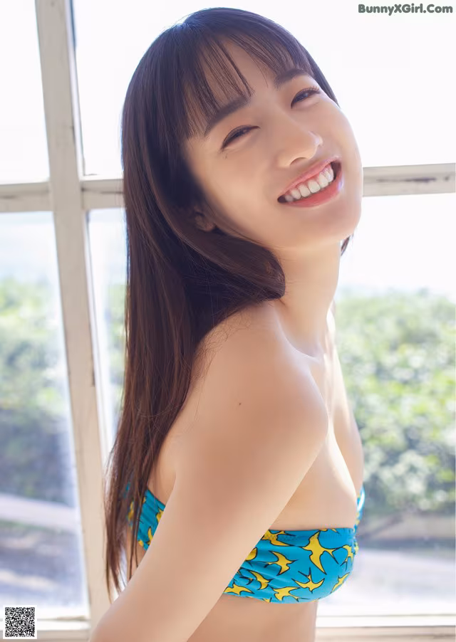A woman in a blue and yellow bikini posing by a window.