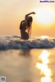 A woman standing in the ocean with her arms outstretched at sunset.