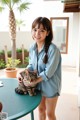 A woman standing next to a table with a cat on it.