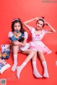 Two young women sitting next to each other on a red background.