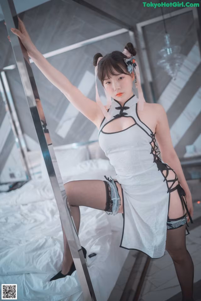 A woman in a white dress and black stockings posing on a bed.