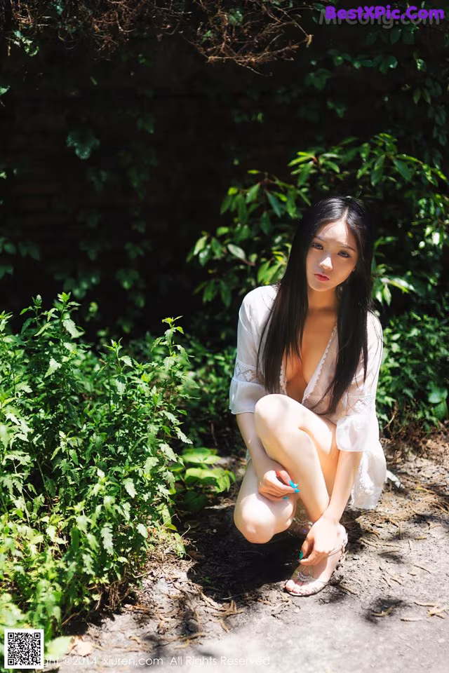A woman in a white dress crouching down in the woods.