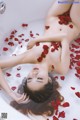 A naked woman laying in a bathtub filled with rose petals.