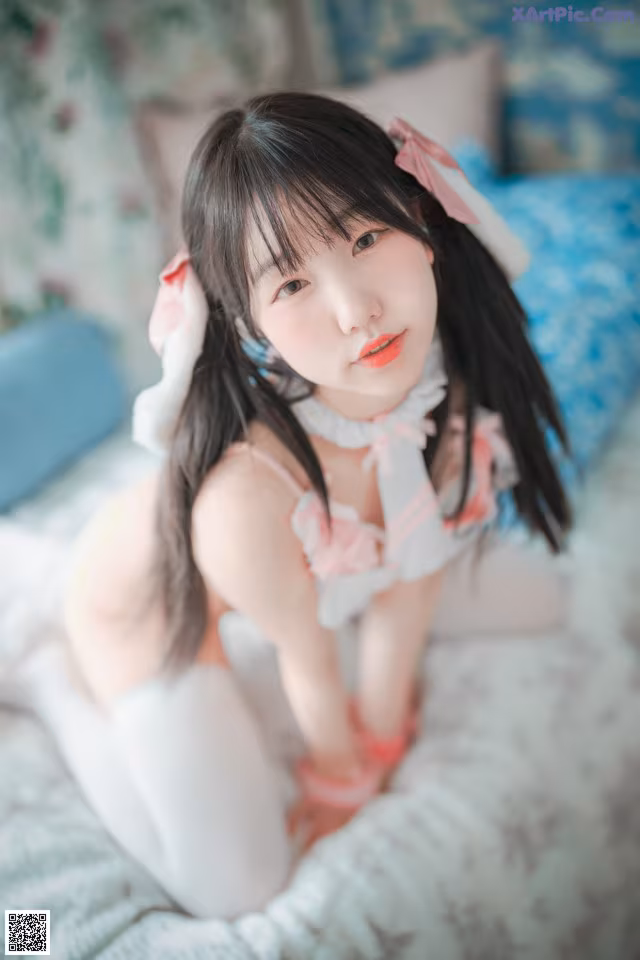 A woman in a pink and white outfit sitting on a bed.