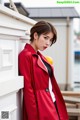 A woman in a red coat leaning against a wall.