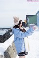 A woman in a blue jacket and hat standing in the snow.