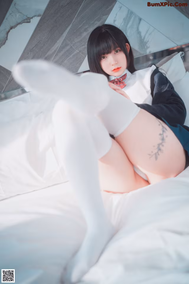 A woman in white stockings and a bow tie laying on a bed.