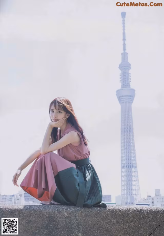 A woman sitting on a wall in front of a tall tower.