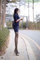 A woman in a blue dress standing on a sidewalk looking at her phone.