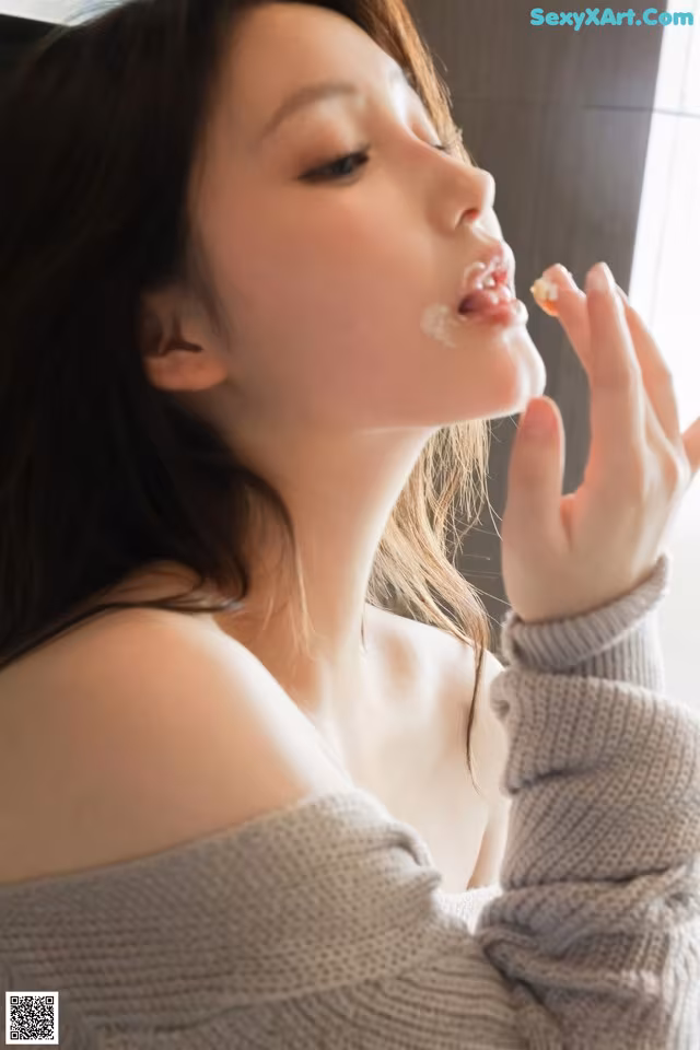 A woman in a gray sweater is eating a piece of food.