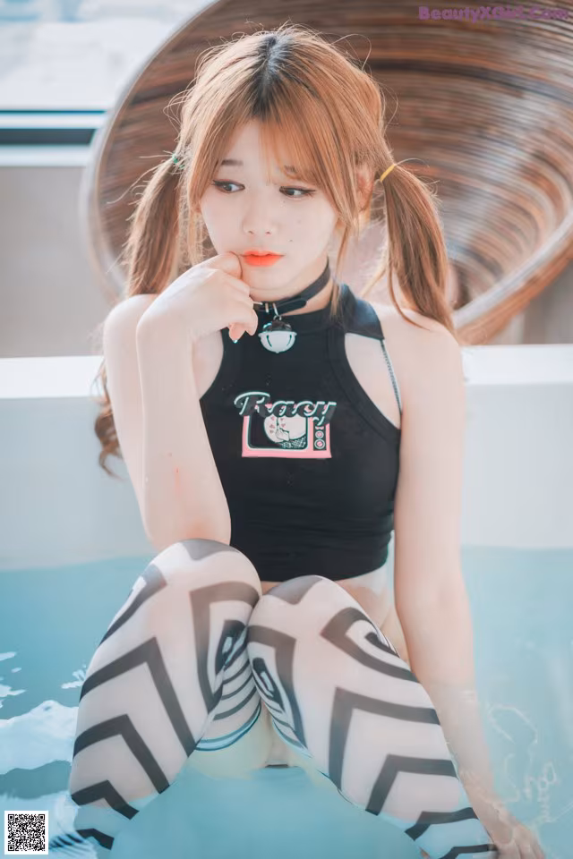 A woman sitting in a bathtub with her hand on her chin.