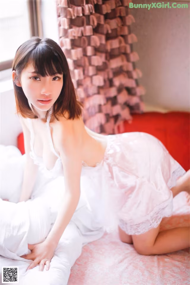 A woman in a white dress sitting on a bed.