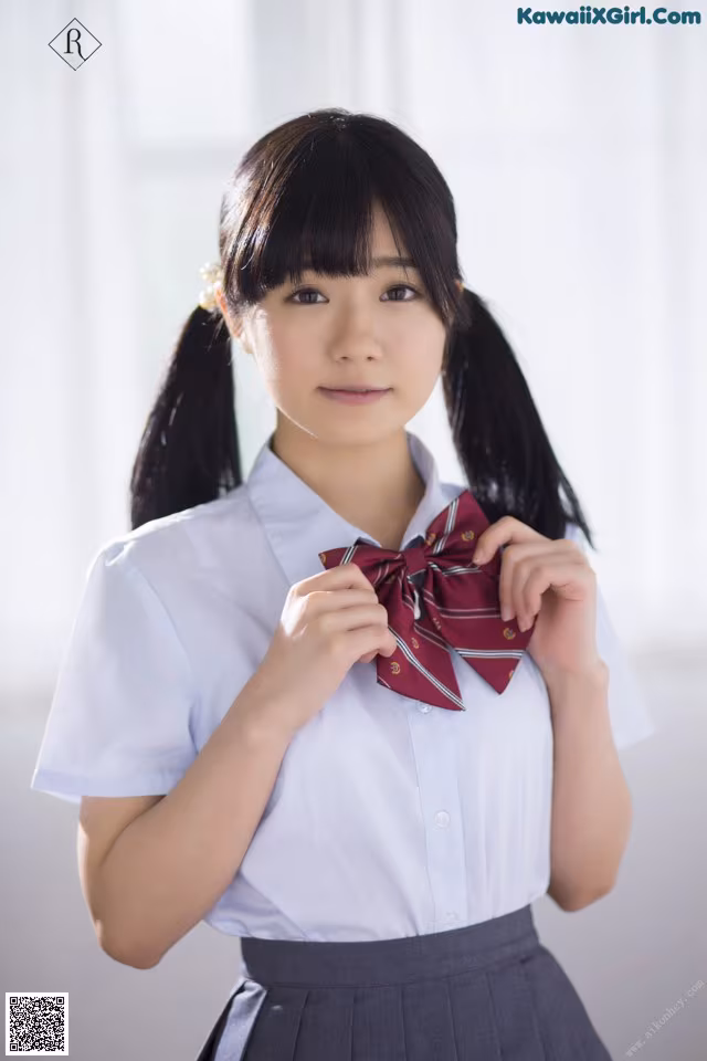 A young woman in a school uniform adjusting her bow tie.