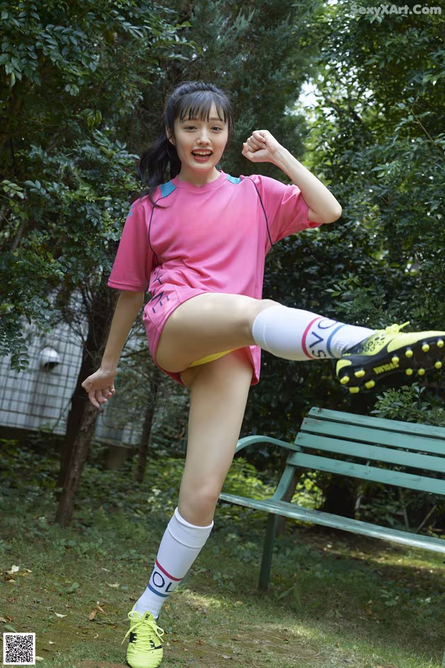 A woman in a pink shirt and yellow shorts kicking a soccer ball.