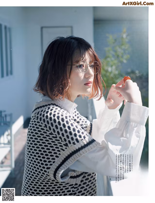 A woman wearing glasses and a white shirt is holding an orange.